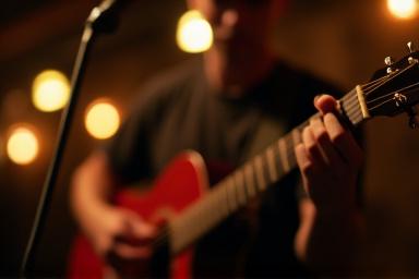 Person playing an acoustic guitar during a live music event at Cedar & Sip